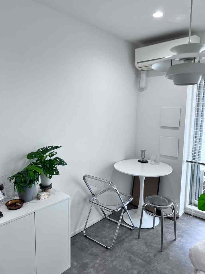 A white and gray toned dining room featuring a minimal round dining table and transparent chairs creating a clean atmosphere
