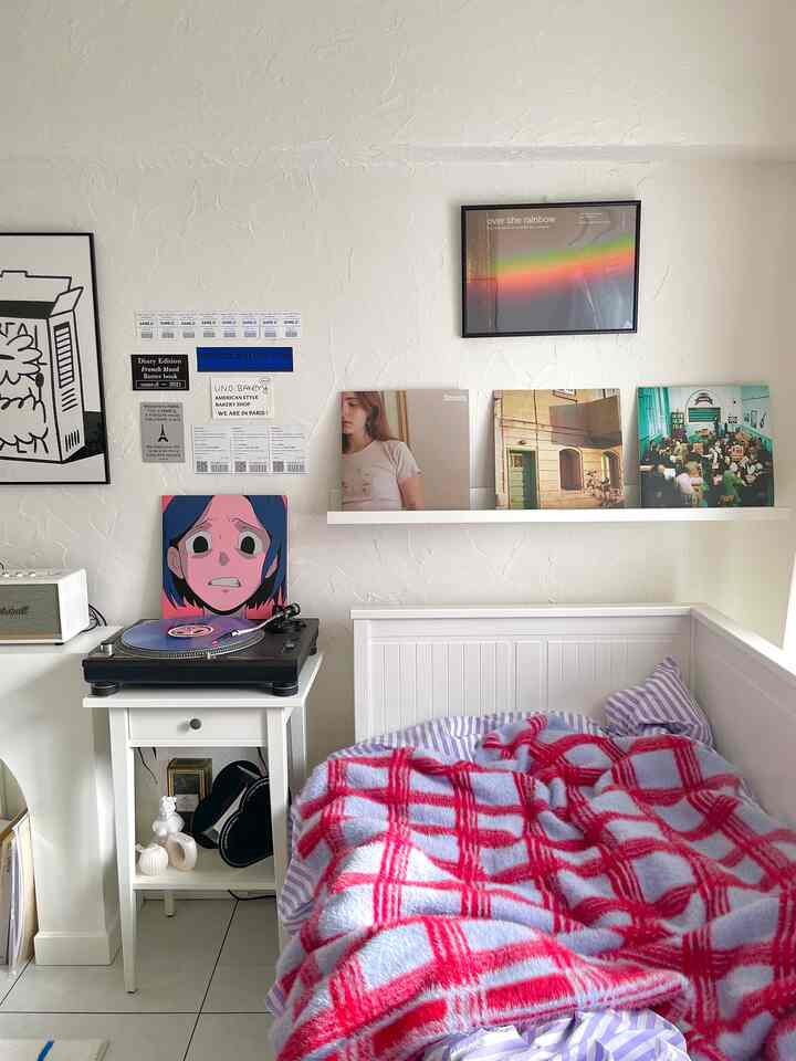 Bright white-toned compact studio bedroom featuring wall posters and checkered bedding with a simple, natural atmosphere