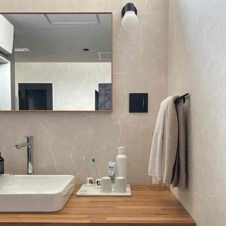 ベージュの壁とナチュラルな木目調のバスルーム、白い洗面台とタオルがすっきりと配置されたシンプルなインテリア