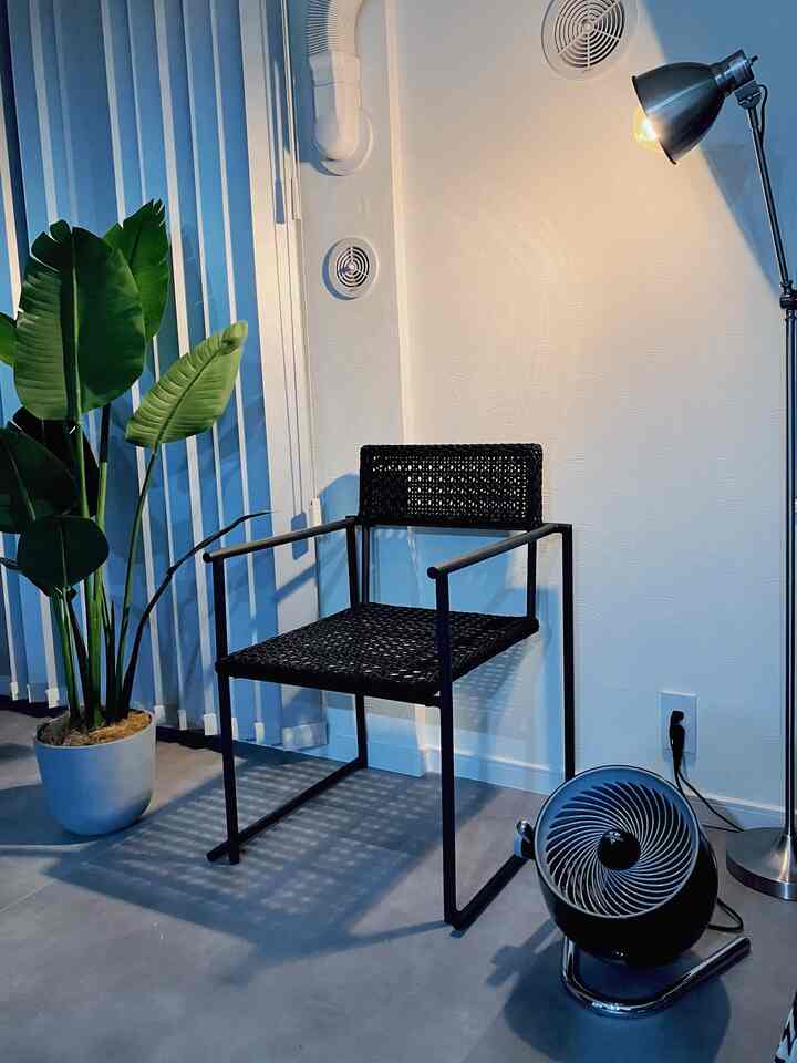 グレーの床と白い壁に、黒のフロアランプと椅子、緑の植物が配置されたシンプルなリビングの雰囲気のあるインテリア