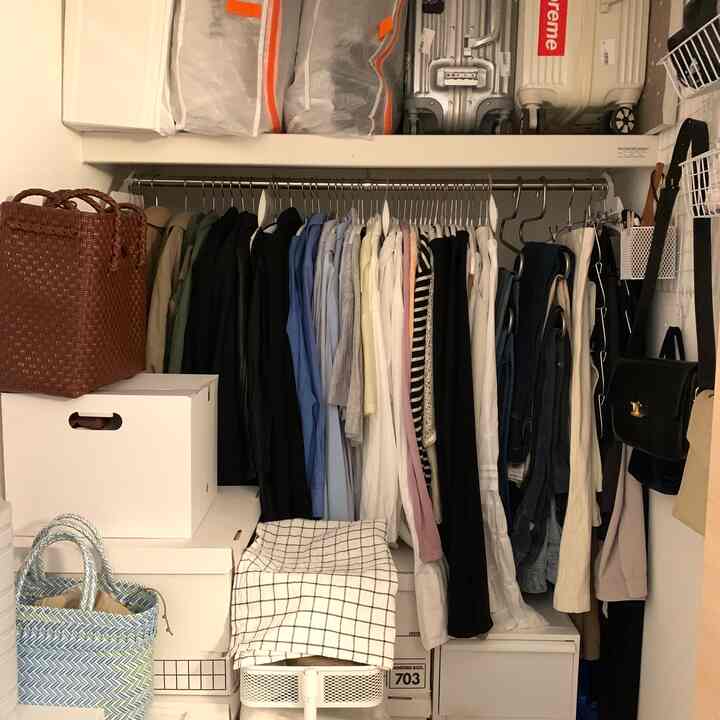 White and natural toned closet space featuring organized storage boxes and hanging clothes in a practical closet interior