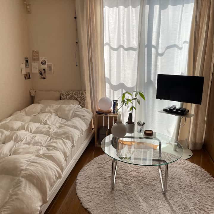 白と茶色のワンルーム寝室、透明な円形テーブルとテレビ台が配置された自然な雰囲気のある居心地の良い空間