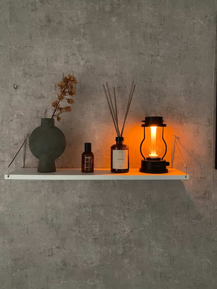 ナチュラルな色調の壁に白い棚が設置され、ディフューザー、ランタン、ドライフラワーが置かれた雰囲気のあるインテリア