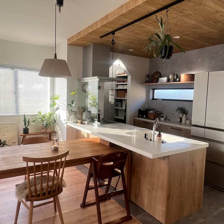 木目調とホワイトの調和した明るく自然なキッチンとダイニング、木製テーブルとペンダントライトが配置された印象的な空間