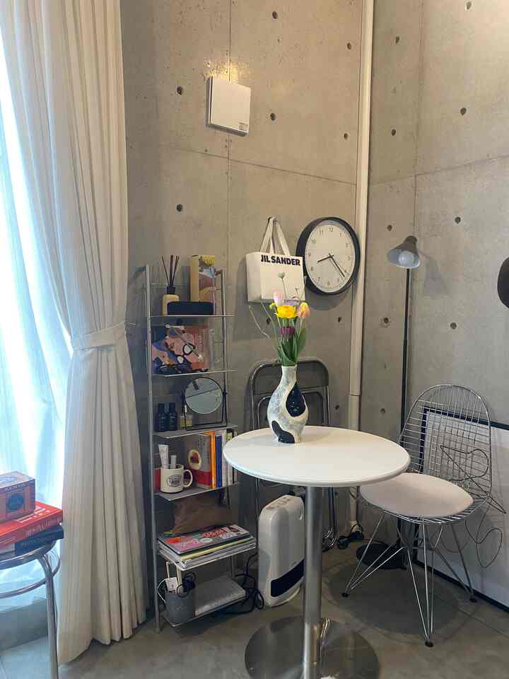 Modern small dining nook with concrete walls and white round table, decorated with flower vase and metal shelving