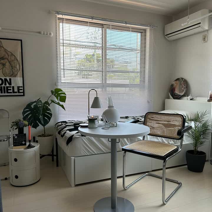 Small bedroom in white and natural tones featuring a rattan chair and plants creating a cozy atmosphere