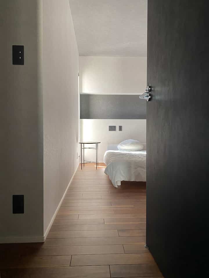 ホワイトとブラウンのナチュラルカラーの寝室、シンプルなサイドテーブルと木目調の床が調和するモダンなインテリア