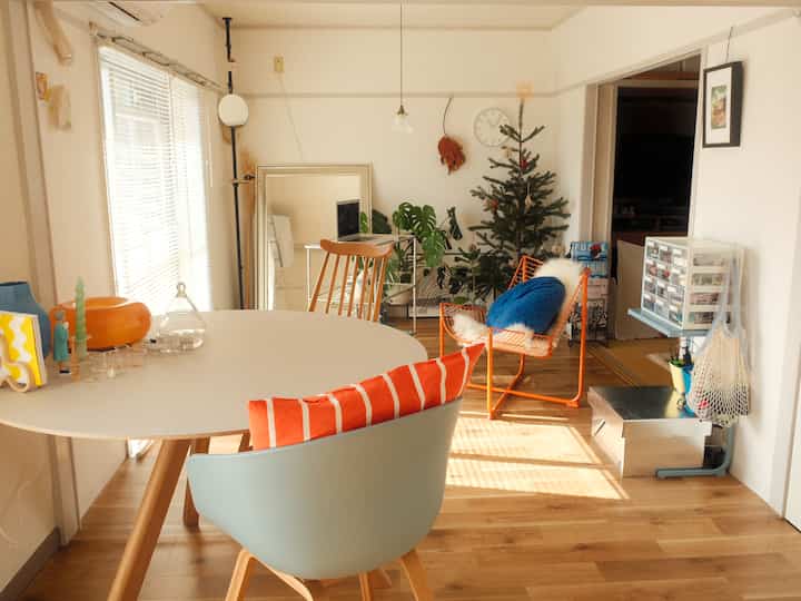 ナチュラルな色調の木製フローリングとオレンジ色のダイニングチェアが配置されたリビング兼ダイニングルームの温かみのある空間