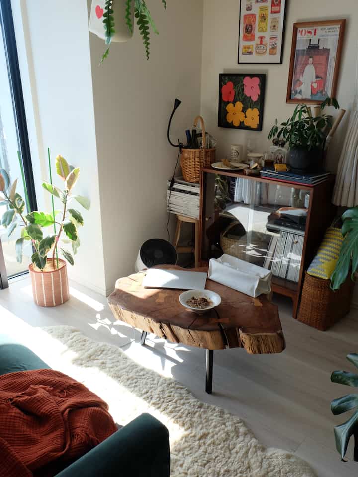Wood tone natural-lit wide living room featuring a rustic coffee table, cabinet, and plants creating a cozy atmosphere