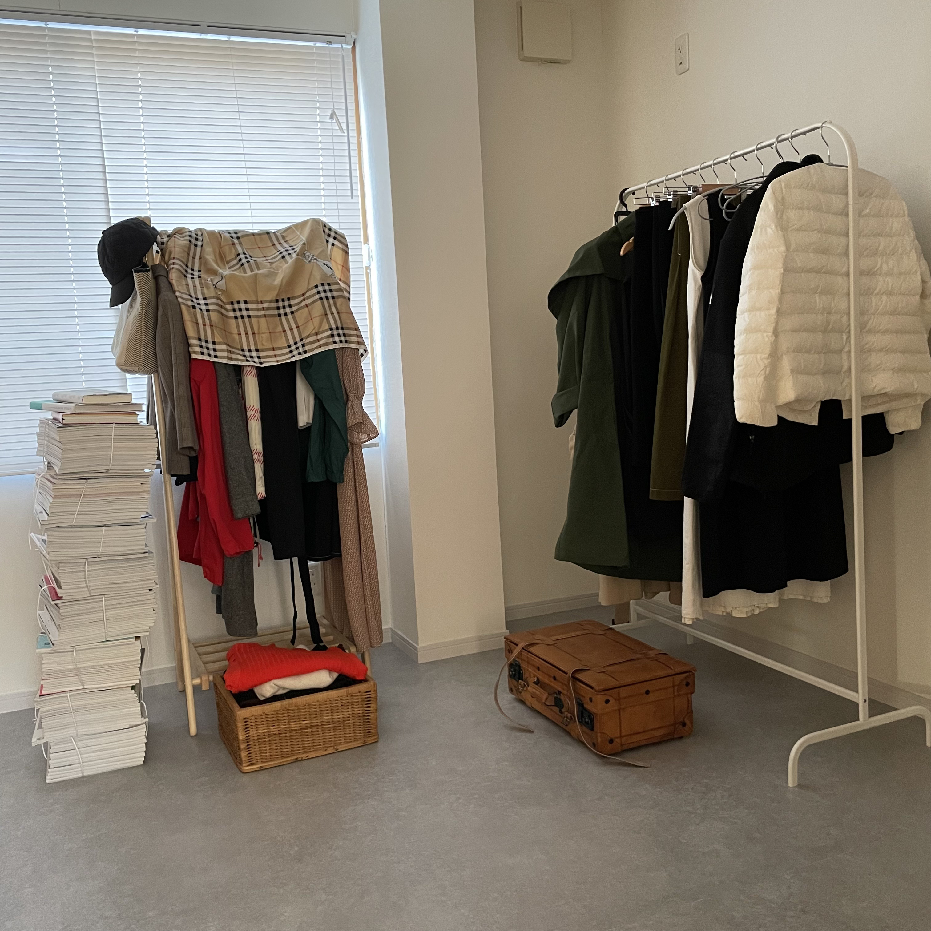 White-walled and gray-floored walk-in closet for two-person household featuring clothes racks and cluttered magazine stacks