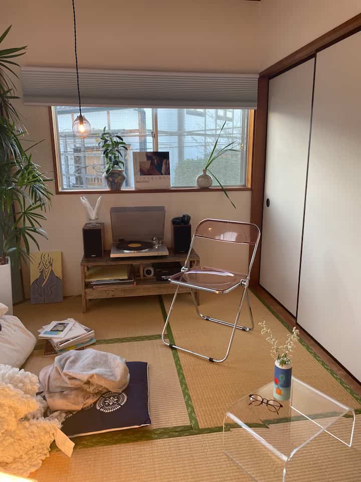 Natural tone 6-tatami Wa-Modern room with tatami flooring, transparent plastic chair, wooden furniture, and blinds at window creating cozy atmosphere