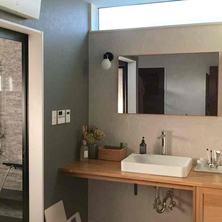 グレーの壁と木目調の洗面台が配置されたナチュラルな雰囲気のバスルームのインテリア