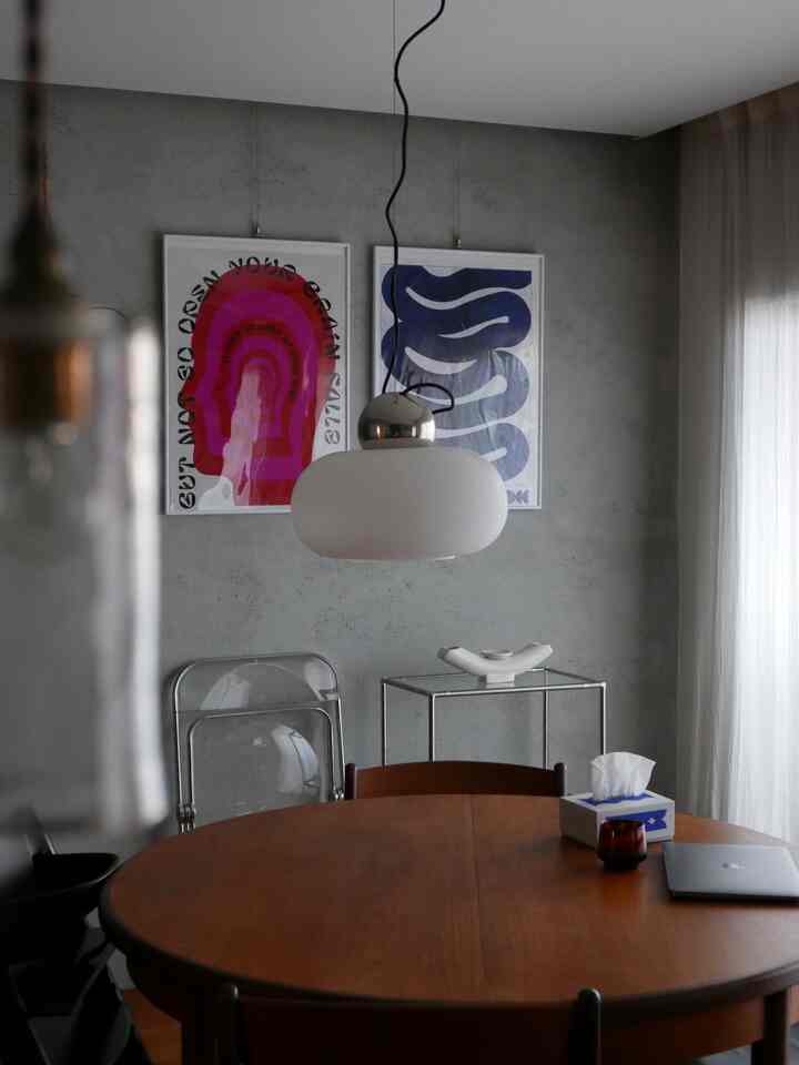 グレーの壁と丸い木製のダイニングテーブル、ペンダントライト、2枚のポスターが置かれたモダンなリビングスペース