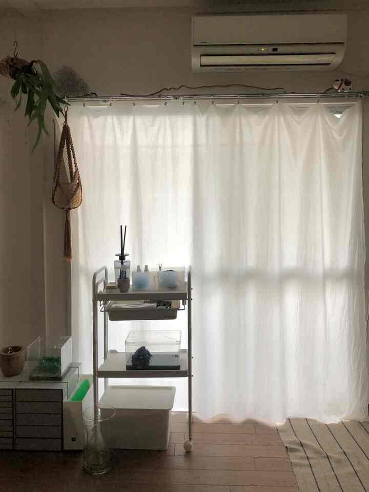 白いカーテンとナチュラルな木目調の床が特徴的な狭い部屋、すっきりとした収納が印象的な空間