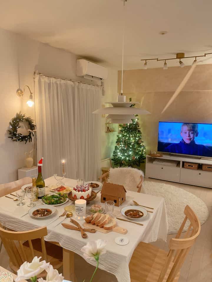 ナチュラルな色調のリビングとダイニング、クリスマスツリーと温かみのあるホームパーティの食事が配置された居心地の良い空間