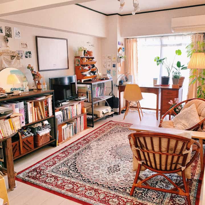 White walls and brown wooden furniture blend in a living room featuring a Persian patterned rug and plants creating a natural home office space