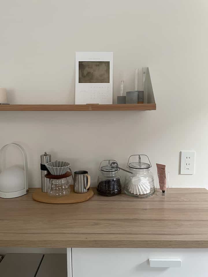 白と木目調が調和した清潔感のあるキッチン空間、テーブルランプとハンドドリップコーヒーセットが置かれている印象的なインテリア