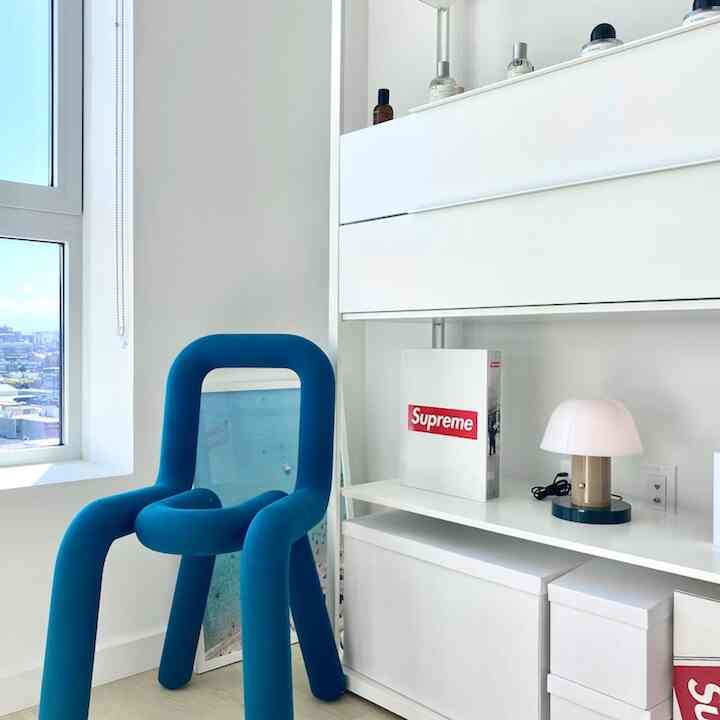 White-toned small living space featuring a blue bold armchair and table lamp, creating a simple atmosphere