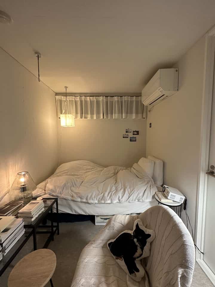 白を基調とした寝室、ベッドとソファ、猫のクッション、照明およびプロジェクターが配置された落ち着いたインテリア