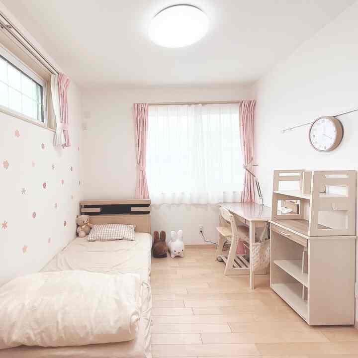 ナチュラルな色調とピンクのカーテンが調和する子供部屋、ベッドと学習机が配置された雰囲気のあるインテリア