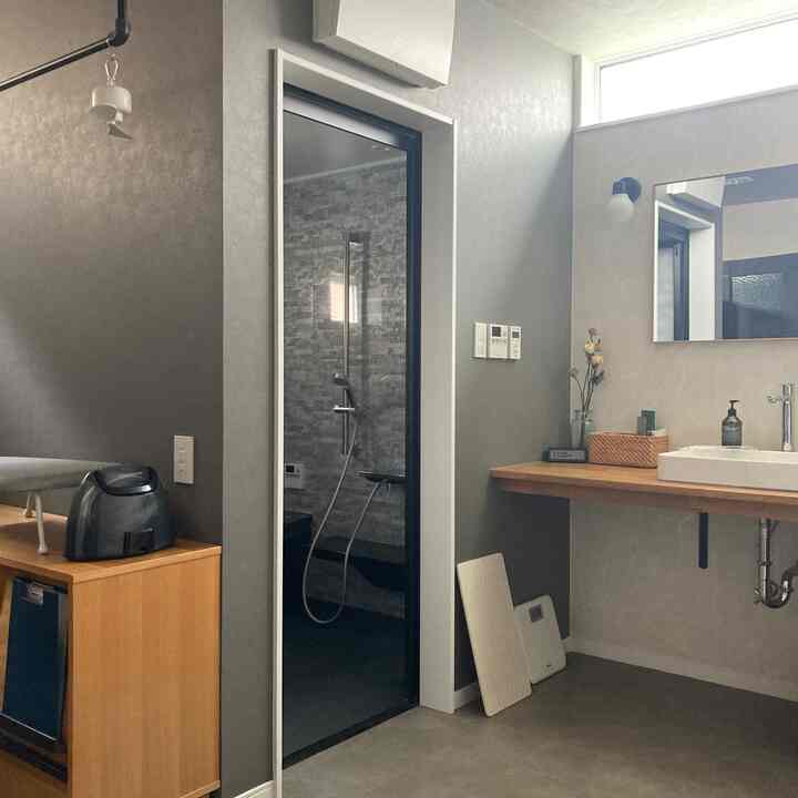 グレーと木目調のモダンな洗面台とシャワーが配置された、清潔感のあるバスルームのインテリア