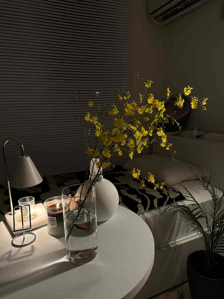 白を基調とした寝室、中央に黄色のオンシジウムの花が置かれたクリアな花瓶と暖かい照明がある印象的な空間