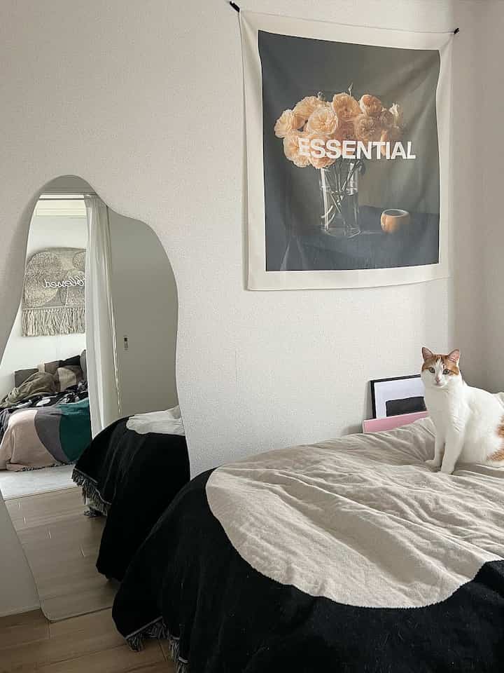 Natural tone 4.5 tatami bedroom with white walls, curved mirror, fabric poster, and a cat on the bed in a minimal and simple setting