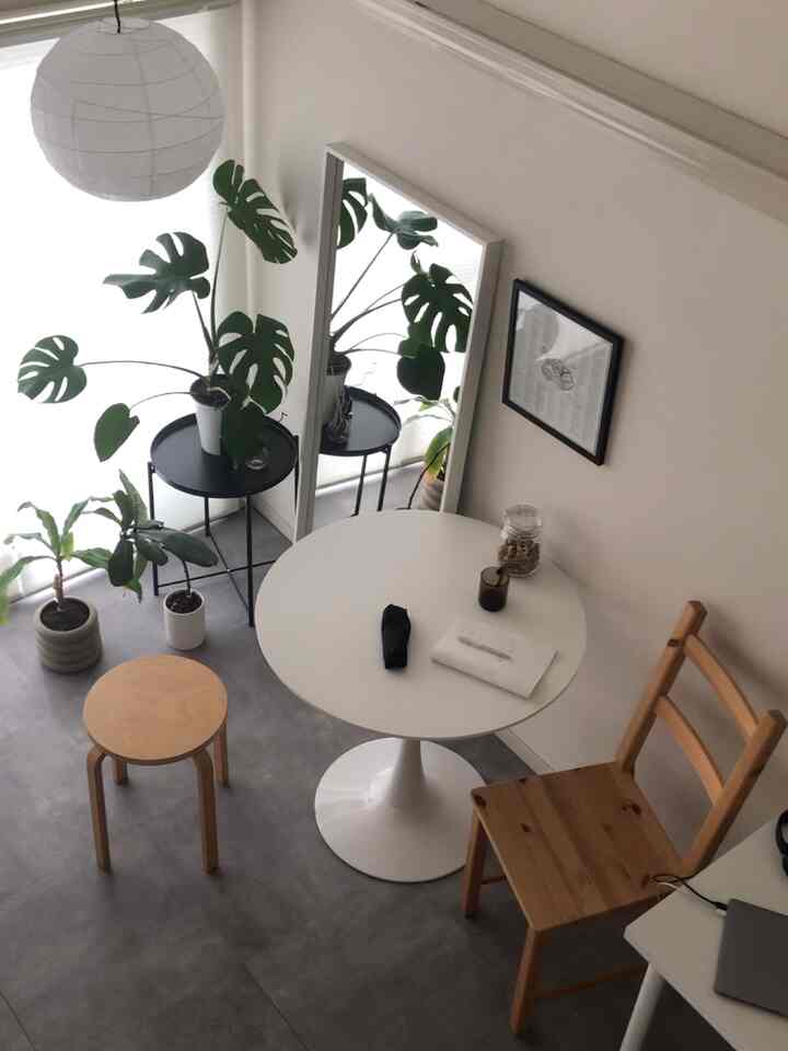 白い壁と木目調家具が調和した狭いカフェ風リビング、全身鏡と植物が配置された温かみのある空間