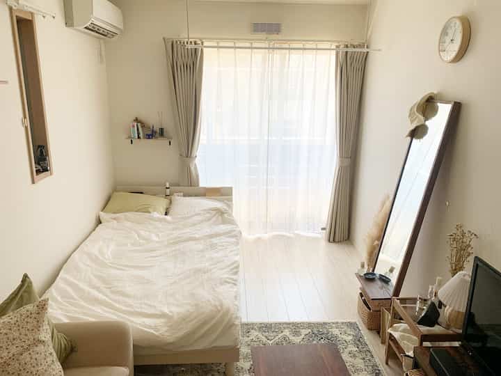 ベージュと白を基調とした小さな寝室、シンプルなベッドと全身鏡が配置された明るく落ち着いた雰囲気のインテリア