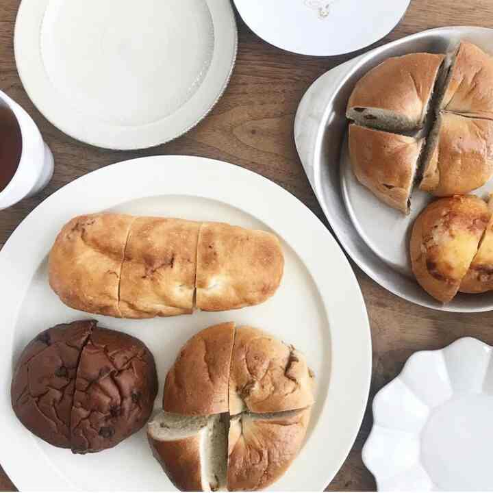 白い食器と様々なパンが並ぶ温かみのあるベージュ色調のダイニングテーブルの雰囲気あるインテリア