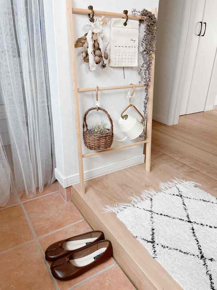 ナチュラルカラーの玄関、木製ラックと白い壁、床に置かれた茶色の靴と白いパターンのラグが配置された雰囲気のある空間