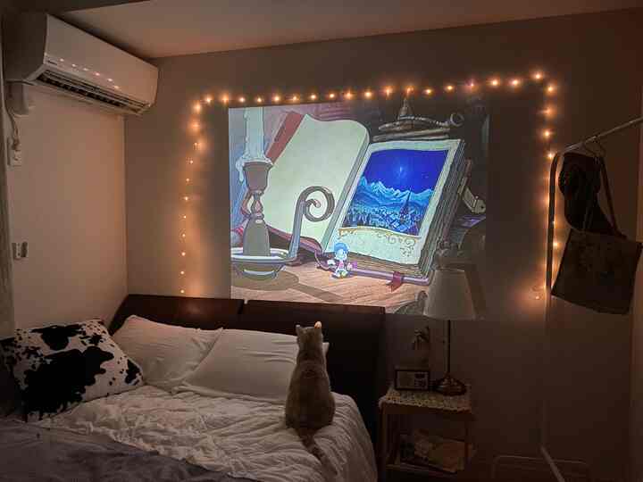 White and gold-lit bedroom featuring a cat sitting on the bed and an animated projection on the wall, creating a cozy atmosphere