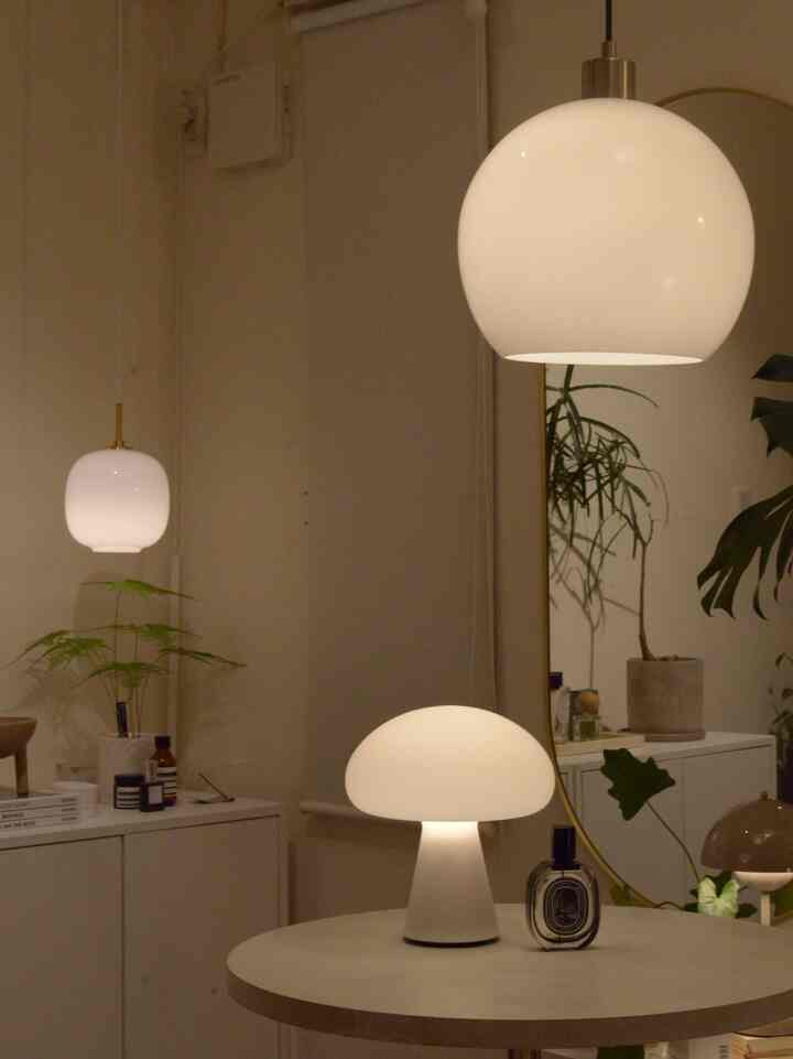 白を基調とした落ち着いた空間、ペンダントライトとテーブルランプ、化粧台や植物が配置されたミニマルなインテリア