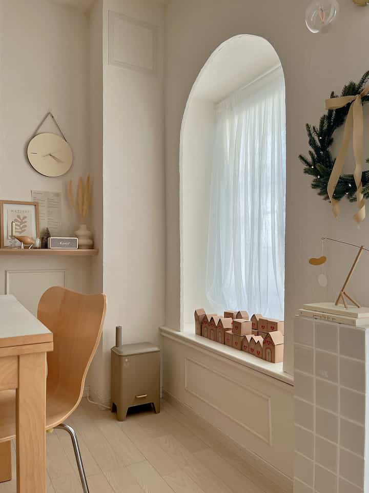 Natural-toned kitchen space featuring beige walls, wooden dining table and chair, white curtains, and advent gift boxes creating a warm atmosphere