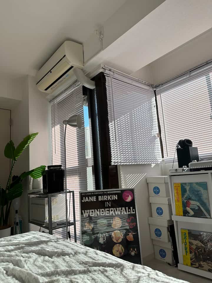 白とシルバーのトーンの寝室、ブラインドや本棚、照明器具が配置されたミニマルで清潔感のある空間