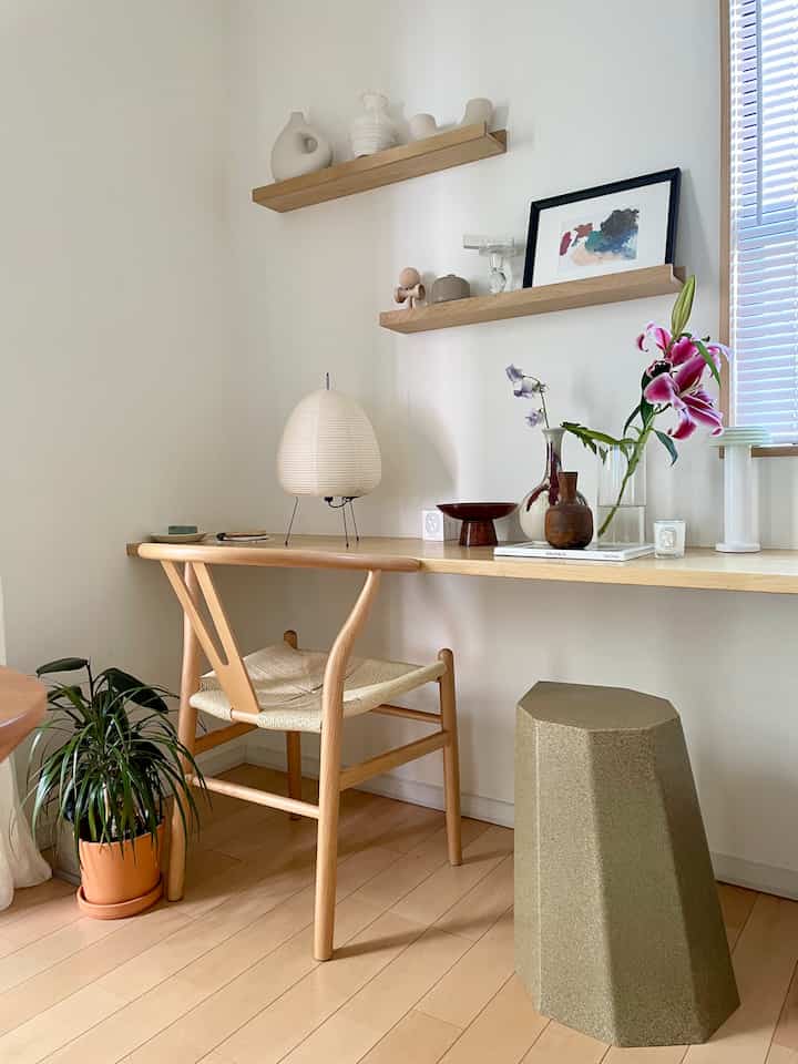 ナチュラルな色調のリビング兼ダイニングスペース、木製のデスクと椅子、スツール、植物、柔らかな照明が調和した雰囲気のあるインテリア