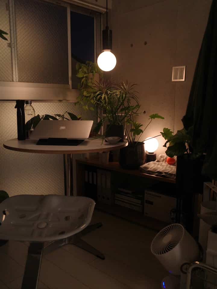 温かみのある照明が灯るホワイトトーンのホームオフィス、植物と丸テーブルが配置された雰囲気のある空間