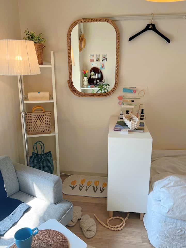 White and wood toned small studio apartment featuring a mirror, storage cabinet, bed, and sofa creating a natural cozy space
