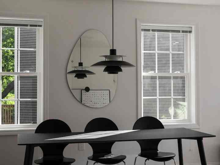 Modern dining room with white walls and windows, featuring black dining table and chairs, Louis Poulsen PH 5 pendant light, and unique wall mirror