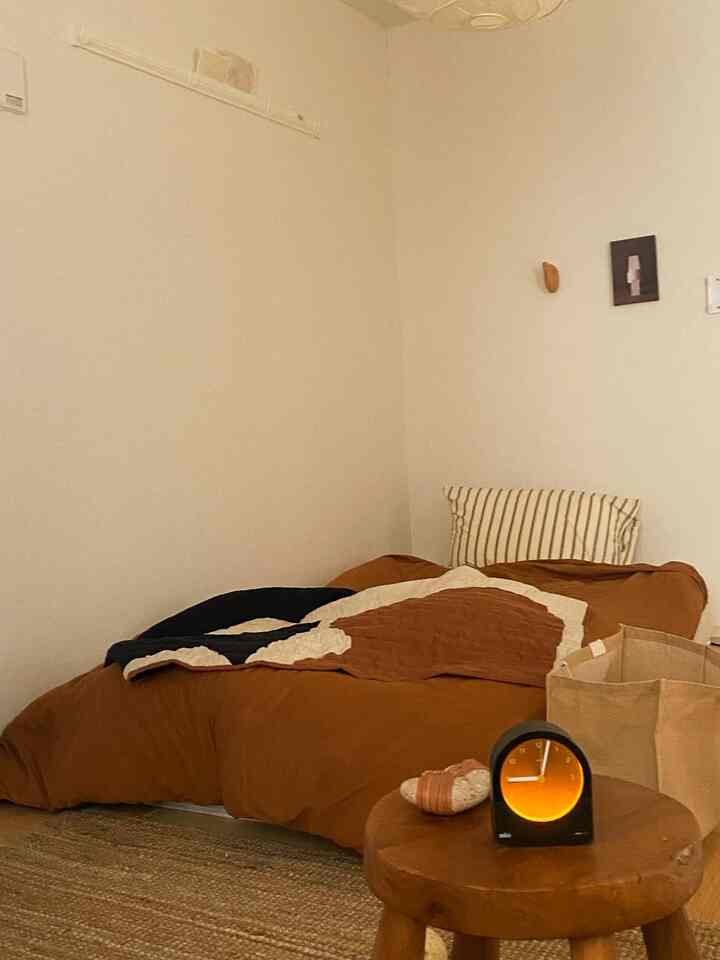 Warm brown and wood tone bedroom with a low bed and ambient analog clock on a wooden stool, creating a cozy space