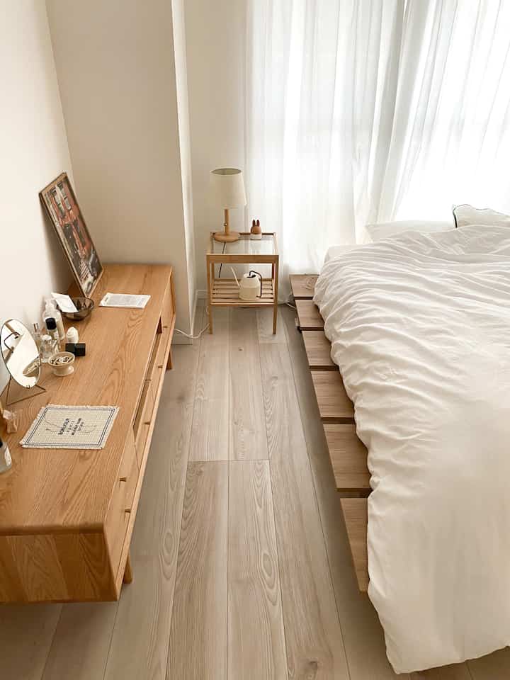A modern bedroom featuring white and wood tones, with a clean bed frame and natural wood dresser arranged for a cozy atmosphere