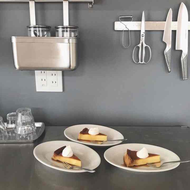 グレーの壁とステンレス製の調理器具が配置されたキッチンのカウンターに、白い皿に載ったケーキの3切れがあるシンプルなキッチンスペース
