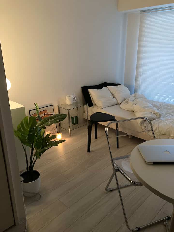 Bright white walls with transparent chair, circular table, cabinet, and green plant in a cozy L-shaped bedroom space