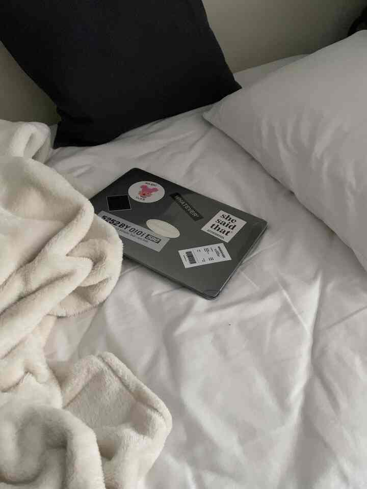 ホワイトの寝具とアイボリーの毛布が置かれた寝室のベッドにノートパソコンが載っている、落ち着いた空間