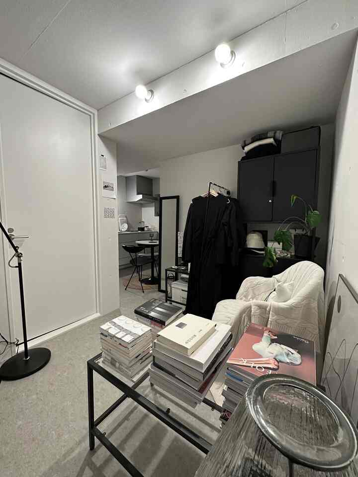 白とグレーのトーンのワンルーム、コーヒーテーブルと居心地の良いアームチェアが配置されたモダンでシンプルな空間