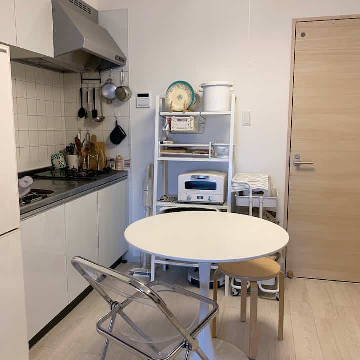 白を基調としたキッチンとダイニング、丸いダイニングテーブルと透明の折りたたみ椅子が配置された清潔感のある空間