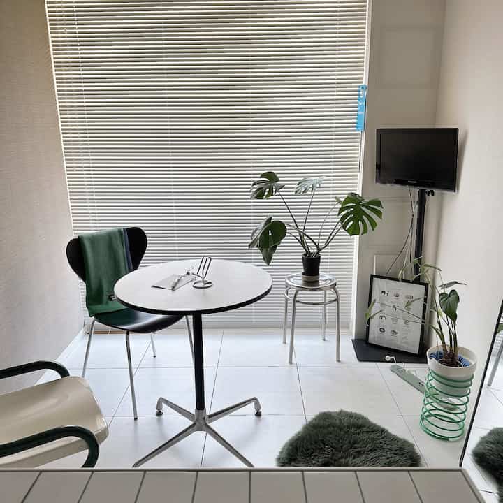 White-toned compact room featuring a small round table with black and cream dining chairs and plants in a modern setting