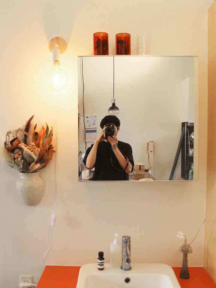 暖かみのあるホワイトとオレンジのトーンが特徴的なバスルーム、中央にシンプルな洗面台と大きな鏡が配置された落ち着いたインテリア