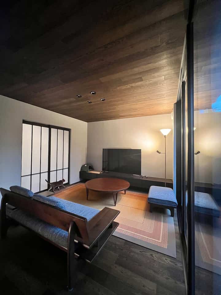 Ivory walls and dark brown wood-tone ceiling highlight a living room featuring a sofa, round coffee table, and rug arranged cozy and minimalistic