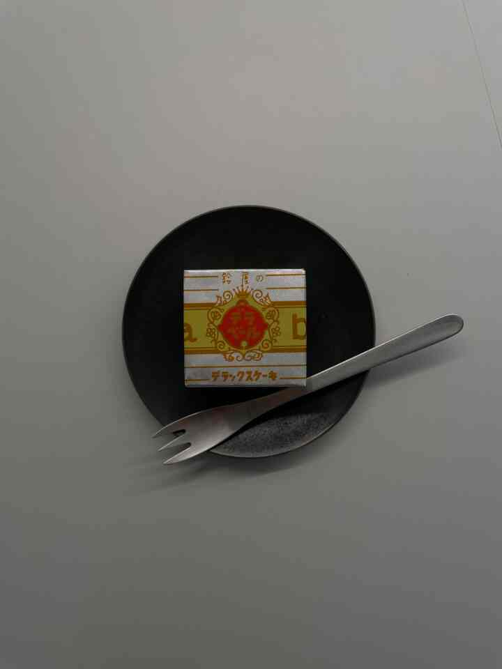 白い背景に黒い皿とステンレスのフォークが配置され、中央に黄色い包装のお菓子が置かれたシンプルな食卓の様子